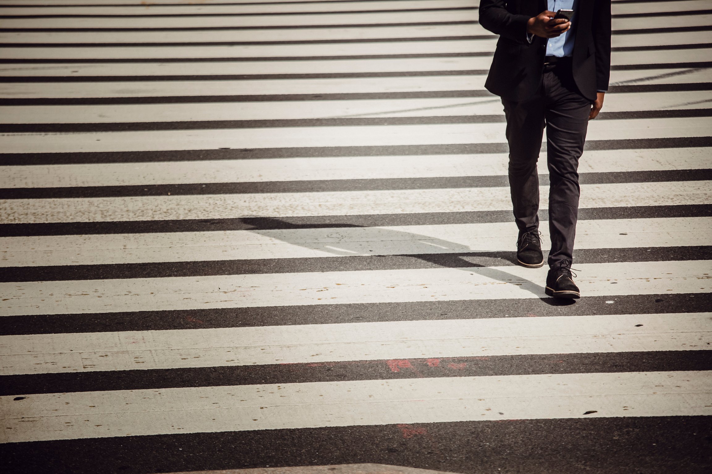 Faceless businessman with smartphone walking on crosswalk in sunlight